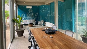 A modern meeting room with a wooden table, chairs, a sofa, and a mural of a meditating figure and marine life. - Elvis Surf Shack at Casa Akaw: a perfect retreat in a sustainable residence (Playa La Saladita)