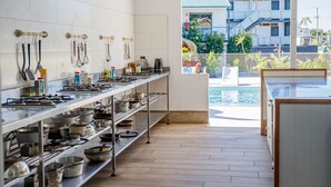 A kitchen with stainless steel appliances and utensils, a wooden floor, and a view of a building and palm trees. - Freedom Backpackers Hostel (Rainbow Beach)