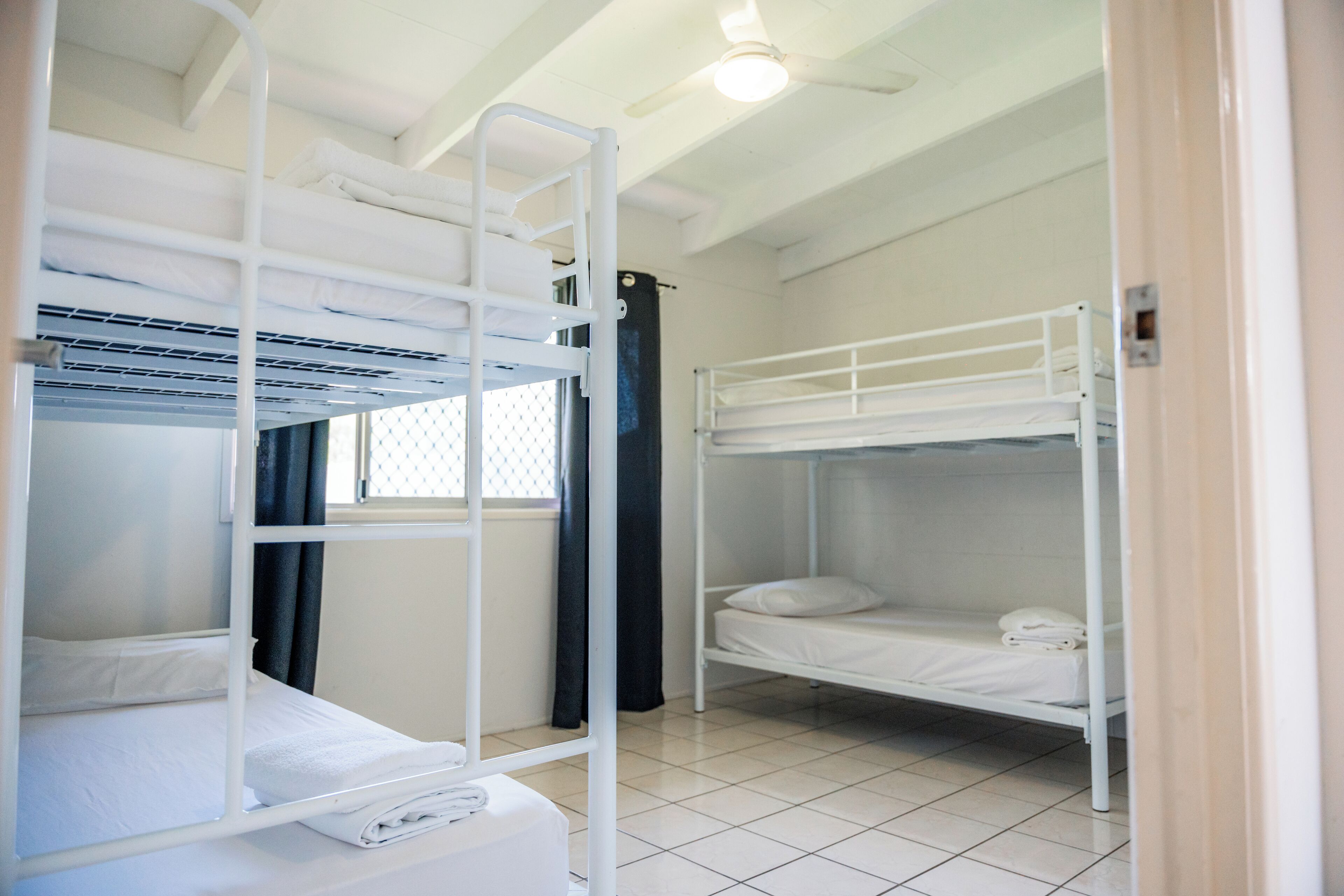 A dormitory room with bunk beds, a window with curtains, and a ceiling fan.