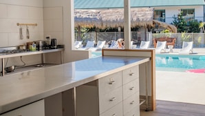 A modern kitchen with a large island, a dining area, and a view of a pool and outdoor seating. - Freedom Backpackers Hostel (Rainbow Beach)