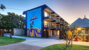 A modern building with a colorful mural, a covered outdoor area, and a well-maintained lawn. - Freedom Backpackers Hostel (Rainbow Beach)