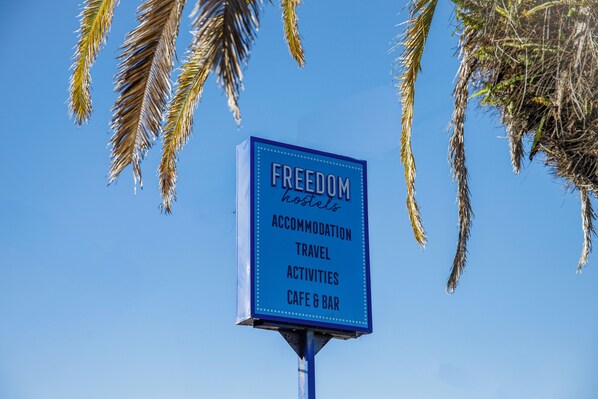 A signboard for 'Freedom Hostels' advertising accommodation, travel activities, and a cafe & bar. - Freedom Rainbow Beach (Rainbow Beach)