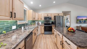 Una cocina moderna con armarios de madera, encimeras de granito, electrodomésticos de acero inoxidable y salpicadero de azulejos verdes.