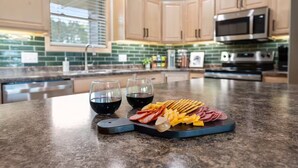 Una cocina con armarios de madera, encimera de granito, microondas y dos copas de vino tinto.
