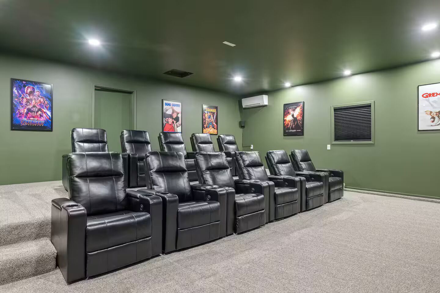 Une salle de cinéma maison avec des murs verts, plusieurs fauteuils inclinables en cuir noir et des affiches accrochées aux murs.