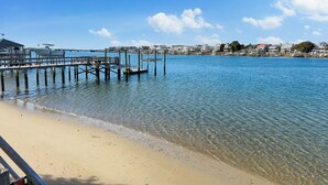 A beach with clear blue water, a wooden pier, and buildings in the background. - Wrightsville Beach Cottage with Stunning Sunset Views, Steps From the Water (Wrightsville Beach)