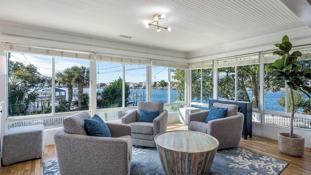 A spacious room with large windows, a round coffee table, and grey upholstered chairs. - Wrightsville Beach Cottage with Stunning Sunset Views, Steps From the Water (Wrightsville Beach)