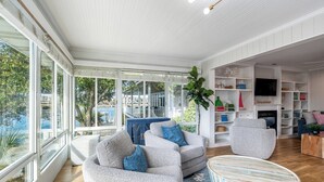 A spacious living room with a large window, a blue accent wall, and a fireplace. - Wrightsville Beach Cottage with Stunning Sunset Views, Steps From the Water (Wrightsville Beach)