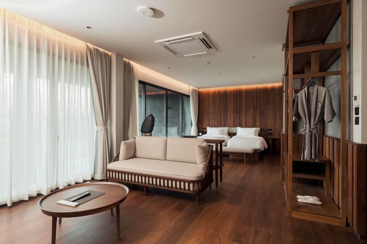 A modern hotel room with a sofa, a small table, a bed, and a wooden wardrobe.