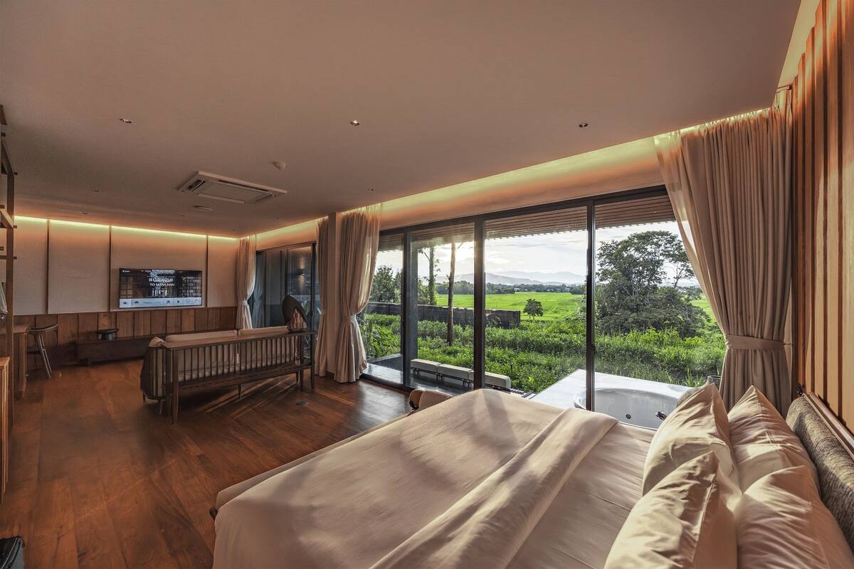 A bedroom with a large bed, a view of the countryside, a small seating area, and a television.