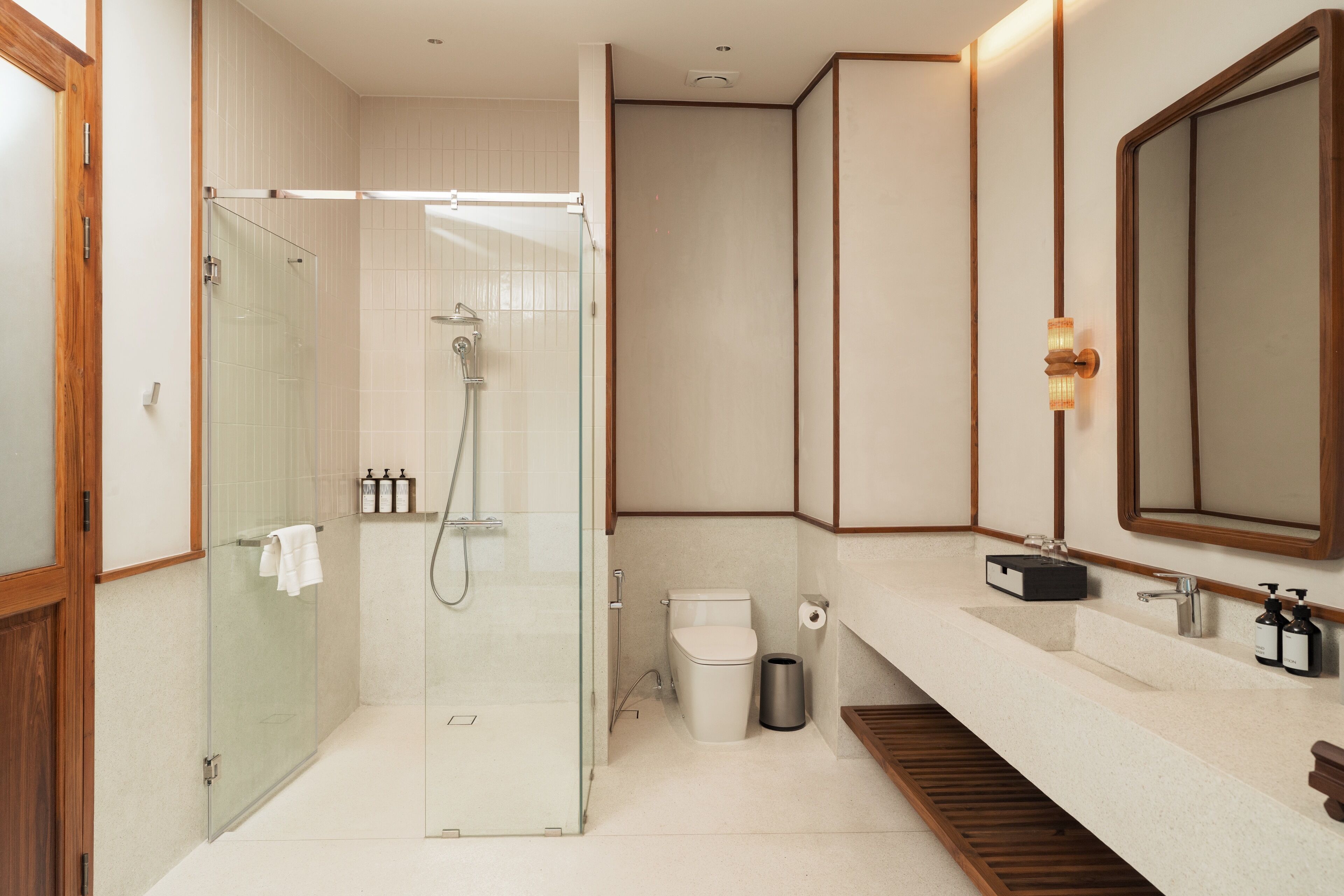 A modern bathroom with a glass-enclosed shower, a toilet, a sink with a mirror, and a trash can.