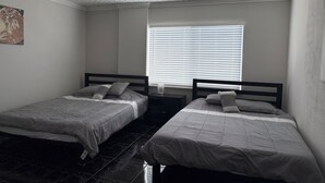 Une chambre avec deux lits simples, une fenêtre avec des stores, un plafond à motifs et un tableau accroché au mur.