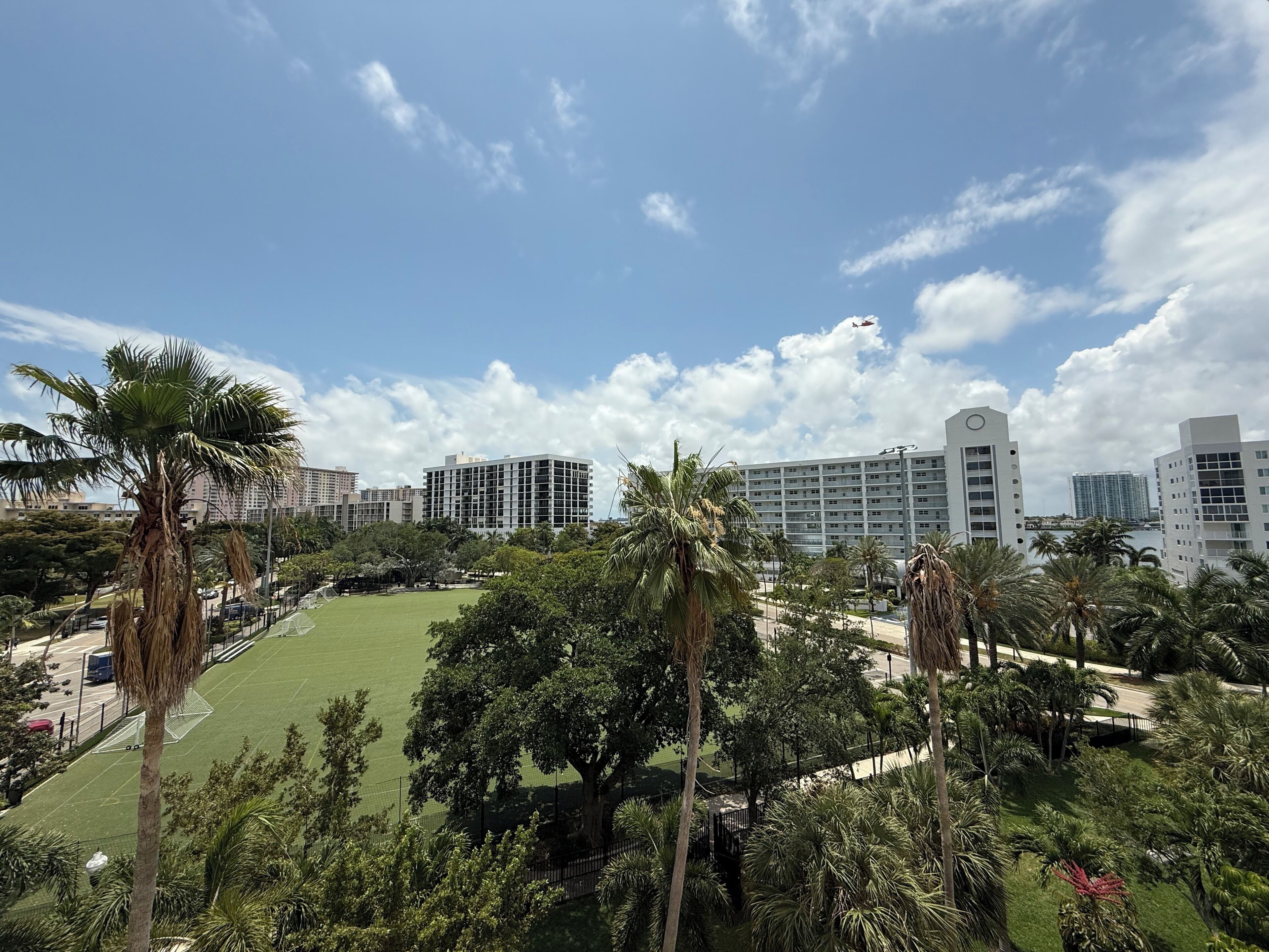 A view of a hotel with multiple buildings, a green lawn, and palm trees.