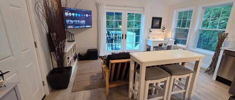 A modern kitchen with a dining area, large windows, and a TV displaying a streaming service.