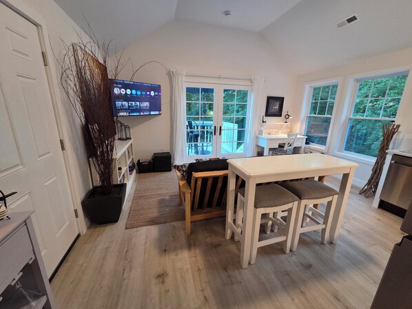 Una cocina moderna con zona de comedor, ventanas amplias y un televisor que muestra un servicio de streaming.