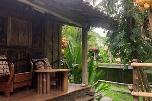 Un espace extérieur aménagé avec des meubles en bois, comprenant une table et des chaises, entouré d’une végétation luxuriante et agrémenté d’une petite piscine.