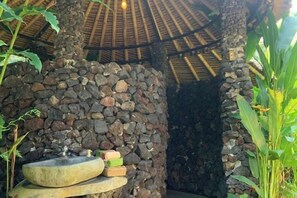Une structure en pierre avec un toit de chaume, un bassin en pierre et une petite pile d’objets.