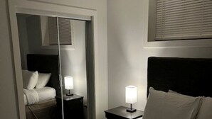 Habitación de hotel con una cama grande, una mesita de noche con lámpara, un armario y una ventana con persianas.