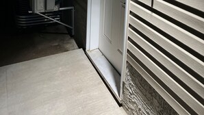 Fachada de una casa con una puerta blanca, un cuadro eléctrico y un aplique de luz exterior.