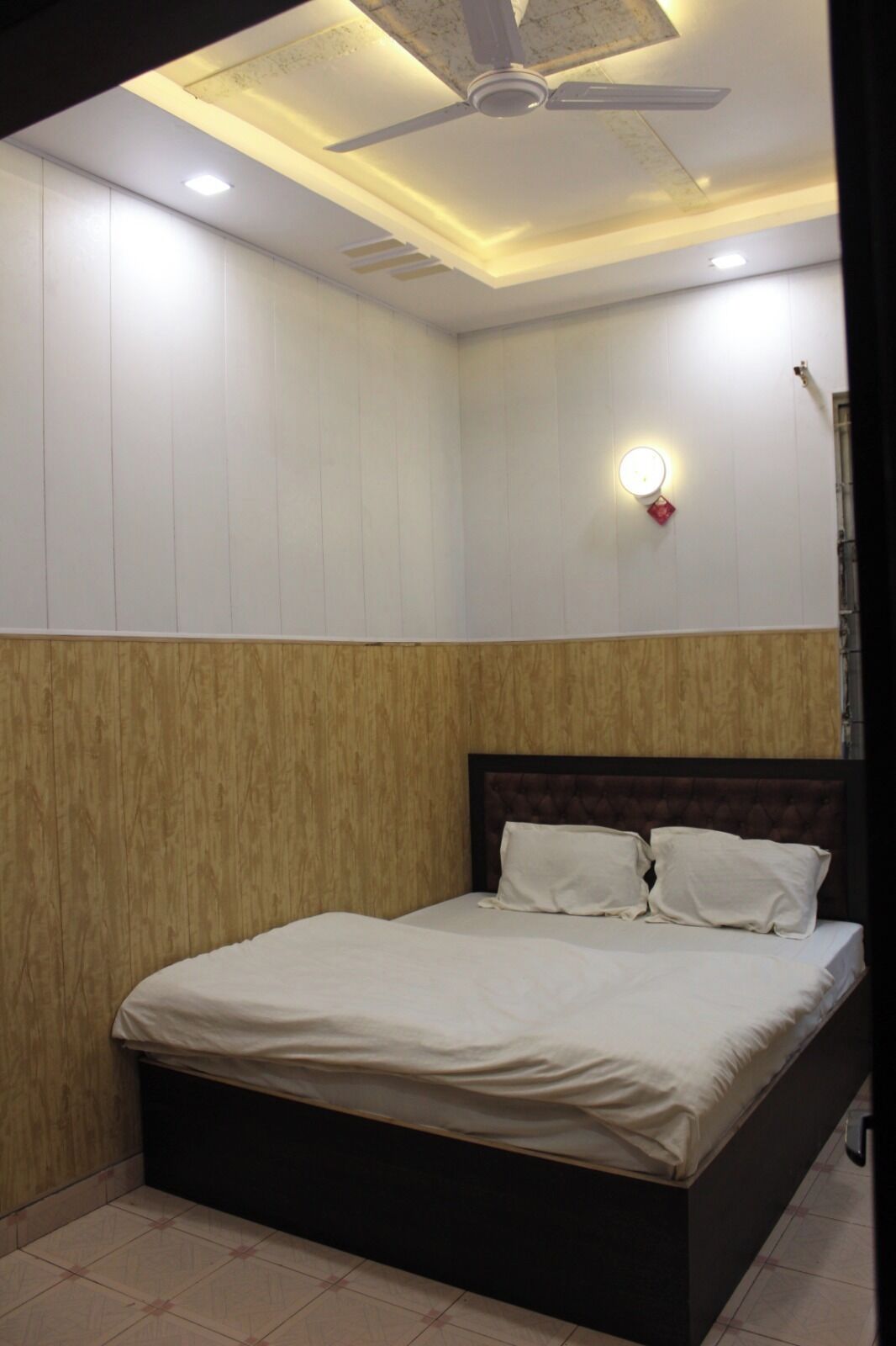 Ein Schlafzimmer mit einem Bett, Holzwandverkleidung, Deckenventilator, Einbauleuchten und einer Wandleuchte.