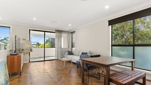 A spacious living room with a wooden herringbone floor, a dining table with benches, a sofa, and a large window with a view of greenery. - Cozy Retreat with Modern Comforts (Entire place) (Camp Hill)