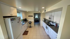 A kitchen with white cabinets, a refrigerator, a microwave, and a stove. There is a door mat on the floor and a small table with a lamp. - 3-bdrm in Ship Bottom. 2 blocks from beach and bars. Surfboards included! (Ship Bottom)