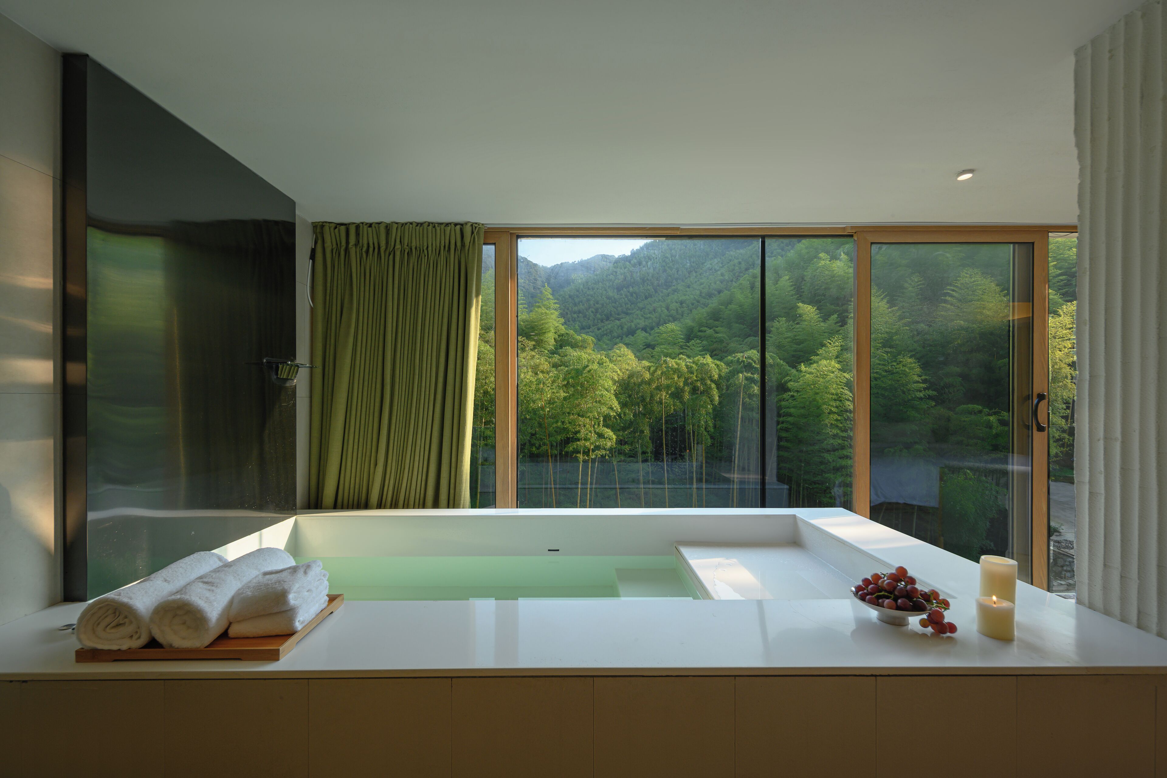 Ein modernes Badezimmer mit einer großen Badewanne, einem Holztablett mit Handtüchern, einer Obstschale und Kerzen.