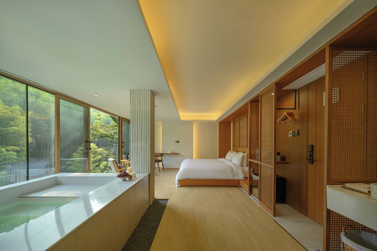 Una habitación de hotel moderna con un ventanal grande, una bañera, una cama y un vestidor.
