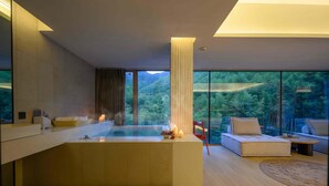 Une salle de bain moderne dotée d’une grande baignoire, d’une douche à parois de verre et offrant une vue sur un paysage boisé.