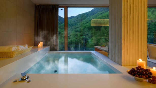 Une salle de spa moderne avec une grande baignoire, un panier en osier rempli de serviettes, un bol de raisins et des bougies.