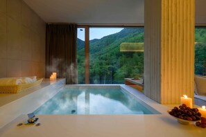 Une salle de spa moderne avec une grande baignoire, un panier en osier rempli de serviettes, un bol de raisins et des bougies.
