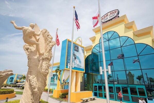 A building with a large glass facade, a sign reading "IRON JON SURF SHOP", and a statue of a surfer.