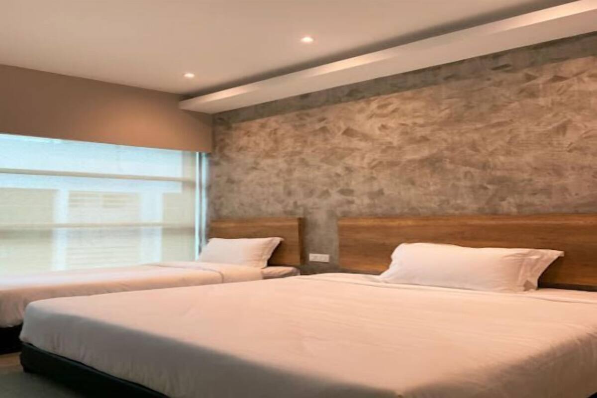 A hotel room with two beds, a stone wall, and a window.