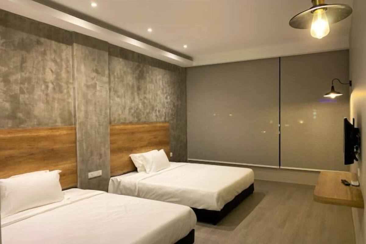 A modern hotel room with two beds, a wooden headboard, a large wardrobe, and a small wooden side table.