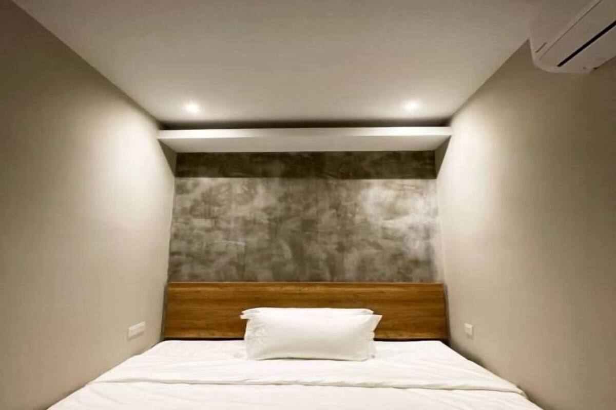 A small, modern bedroom with a single bed, a wooden headboard, and a textured wall behind the bed.