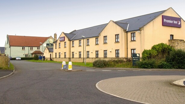 Een hotel met een bord waarop 'Premier Inn' staat en een bord met 'The Stonebrook'. Er staan paaltjes in de weg en een verhard gebied op de voorgrond.