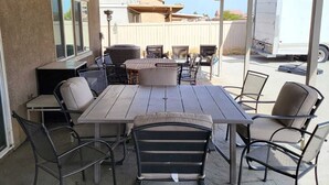 Een terras buiten met een tafel, stoelen, een barbecue en een overdekt gedeelte.