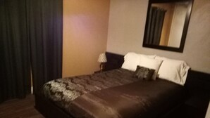 Een net opgemaakt bed met een bedsprei met patroon, een bedlamp en een spiegel aan de muur.