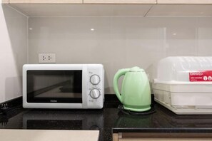 Un microondas, una tetera verde y un recipiente para alimentos sobre una encimera de cocina.