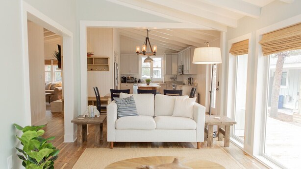 A modern living room with a white sofa, a wooden coffee table, and a dining area with a wooden table and chairs. - Retreat for families, walk to beach, stocked kitchen, pet friendly, fenced yard (Pawleys Island)