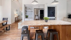 A kitchen with a large island, wooden stools, pendant lights, and a refrigerator. - Retreat for families, walk to beach, stocked kitchen, pet friendly, fenced yard (Pawleys Island)