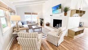 A spacious living room with a fireplace, striped armchairs, a sofa, and a coffee table. - Retreat for families, walk to beach, stocked kitchen, pet friendly, fenced yard (Pawleys Island)