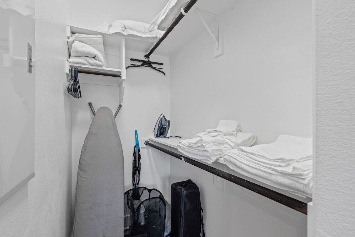 A compact hotel room with a bed, a small ironing board, and a suitcase.