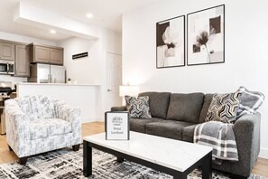 Ein modernes Wohnzimmer mit Sofa, Sessel und Couchtisch. Ein Schild weist auf eine Gästebuchvermietung hin.
