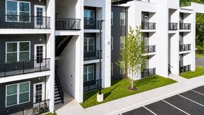 A modern multi-story residential building with balconies, a central staircase, and a small tree in the front yard.