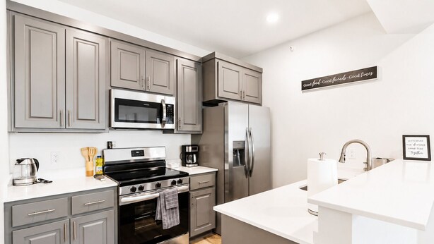 A modern kitchen with grey cabinets, stainless steel appliances, a white countertop, and a black rug.