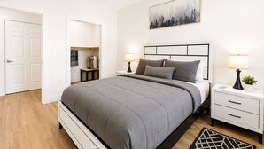 A bedroom with a bed, bedside tables, a nightstand, a painting, and a closet.
