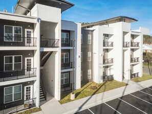 A multi-story residential building with balconies, a central staircase, and a parking lot in front. - Stylish Suite 103 by Downtown & Convention Center! (Hot Springs)