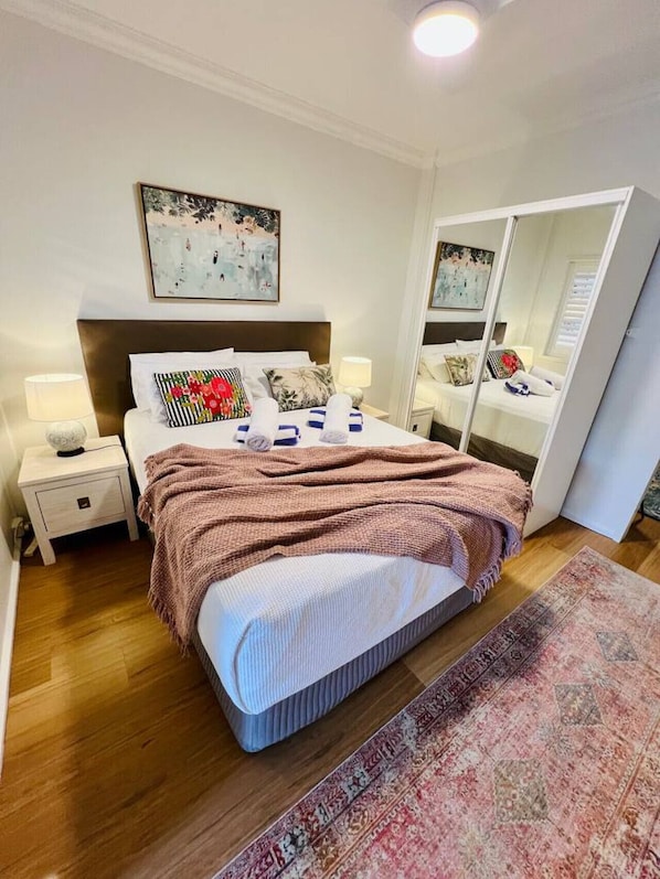 A modern bedroom with a large bed, a bedside table with a lamp, a mirror, and a painting on the wall.