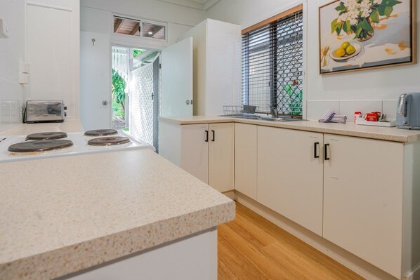 A kitchen with a countertop, cabinets, a window with blinds, and a painting on the wall.